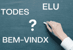 Uma mão com um giz escrevendo em uma lousa. Na lousa, um ponto de interrogação ao centro; à esquerda, "todes" e "bem-vindx" grafados. À direita "elu" grafado.