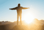 Um homem de braços erguidos em frente ao pôr-do-sol/nascer do sol.
