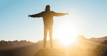 Um homem de braços erguidos em frente ao pôr-do-sol/nascer do sol.