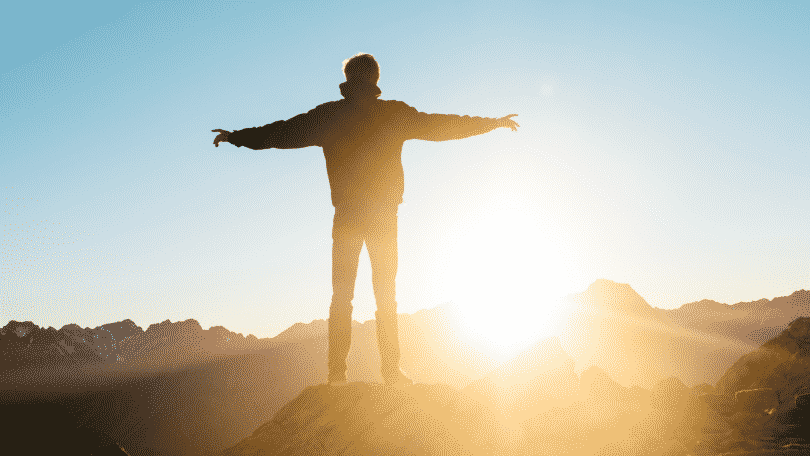 Um homem de braços erguidos em frente ao pôr-do-sol/nascer do sol.