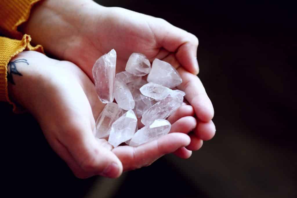 Duas mãos em concha segurando pedaços de quartzo transparente.