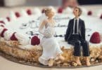 Sobre um bolo, miniaturas de noivos, sendo uma representante de um homem e a outra de uma mulher.