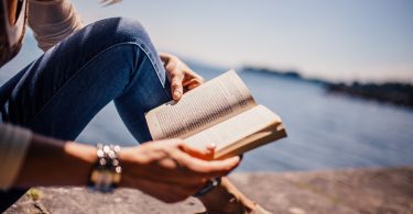 Uma mulher lendo um livro. Ao fundo, um rio.