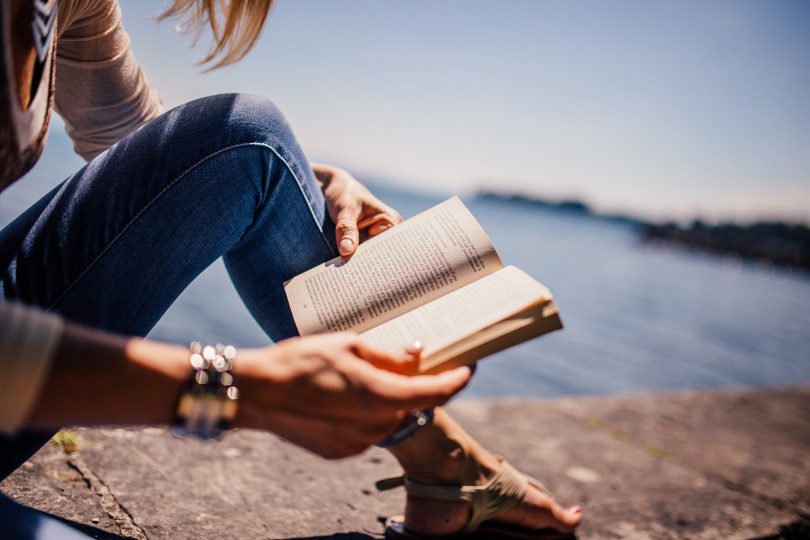 Uma mulher lendo um livro. Ao fundo, um rio.