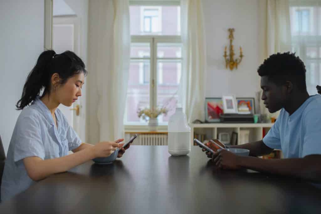 Uma mulher e um homem situados à mesa, cada um, usando um celular