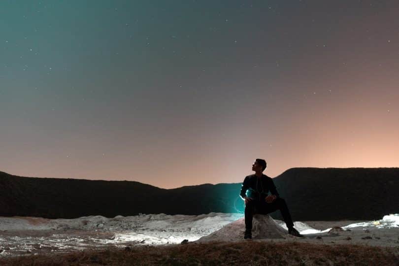 Homem sentado numa pedra observando o céu.