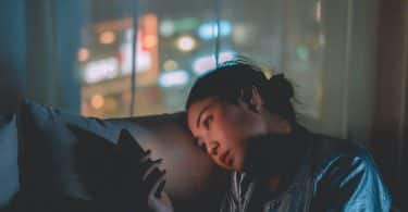 Uma mulher asiática debruçando a cabeça sobre um sofá e observando um celular.