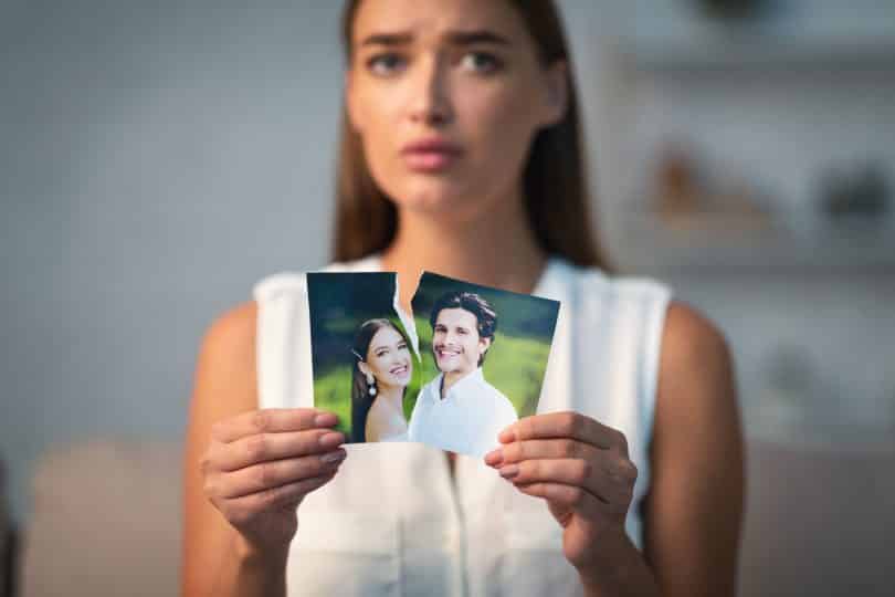 Uma mulher rasgando uma fotografia que tem um homem e uma mulher.