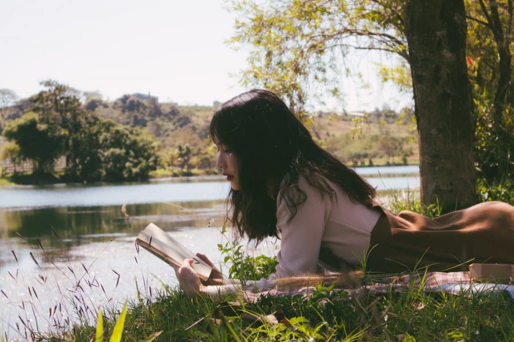 Mulher asiática deitada na grama lendo livro.