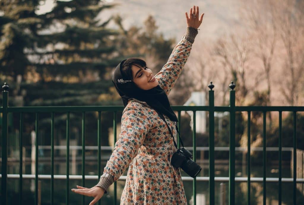 Mulher de hijab e braços abertos enquanto sorri.