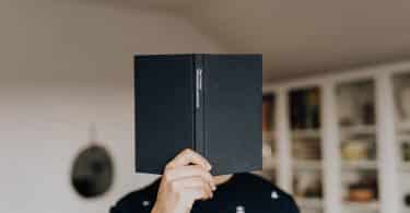 Homem com um livro em frente ao seu rosto