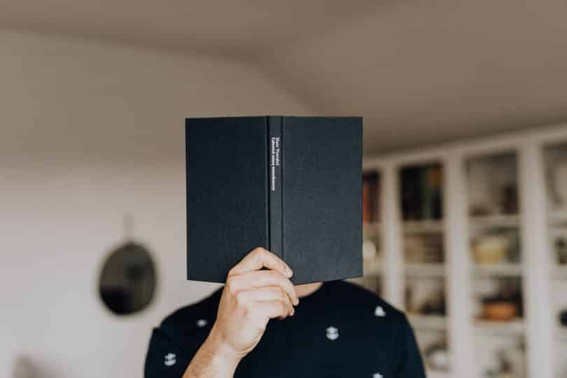 Homem com um livro em frente ao seu rosto