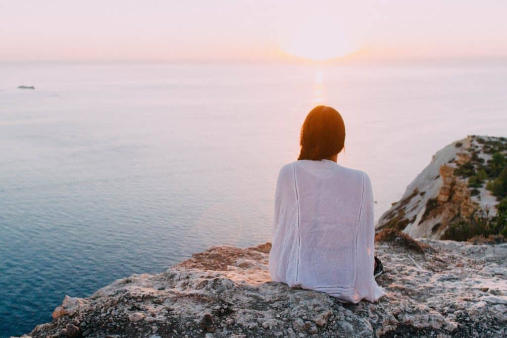 Mulher sentada em uma rocha em frente ao pôr do sol