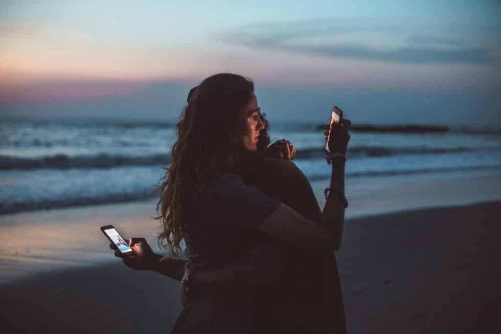 Uma mulher e um homem abraçados olhando, cada um, o seu celular