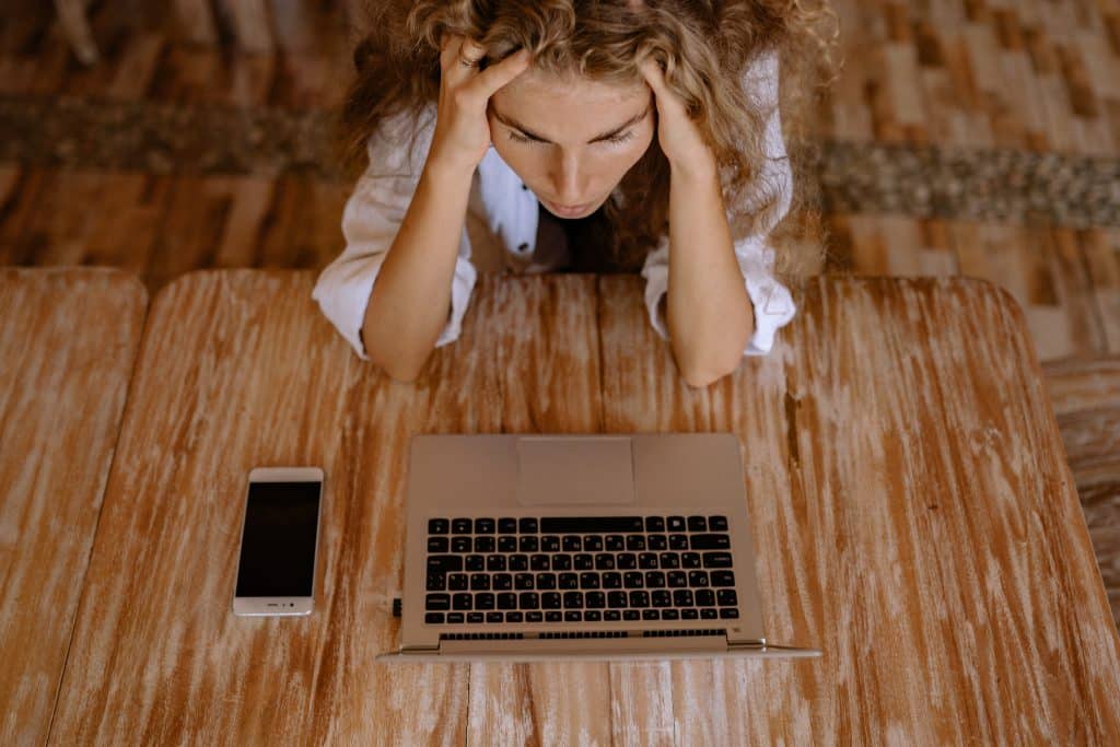 Mulher sentada em frente ao seu laptop com suas mãos na cabeça