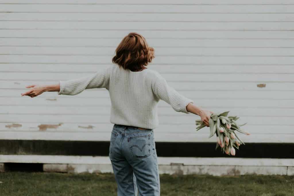 Mulher branca segurando buquê de flores com os braços abertos.