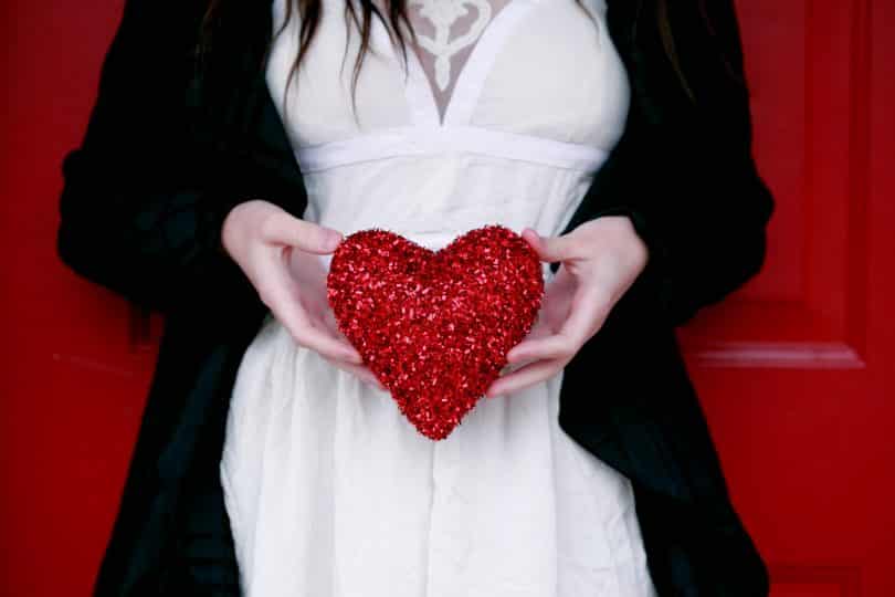 Mulher branca segurando coração vermelho.