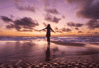 Mulher de braços abertos na praia durante o pôr do sol