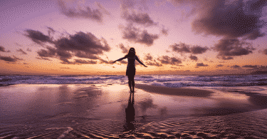 Mulher de braços abertos na praia durante o pôr do sol