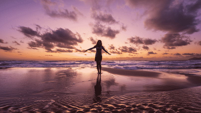 Mulher de braços abertos na praia durante o pôr do sol