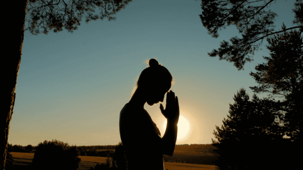 Silhueta de mulher orando durante o por do sol
