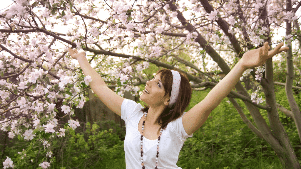 Mulher sorridente de braços abertos observando as flores na primavera