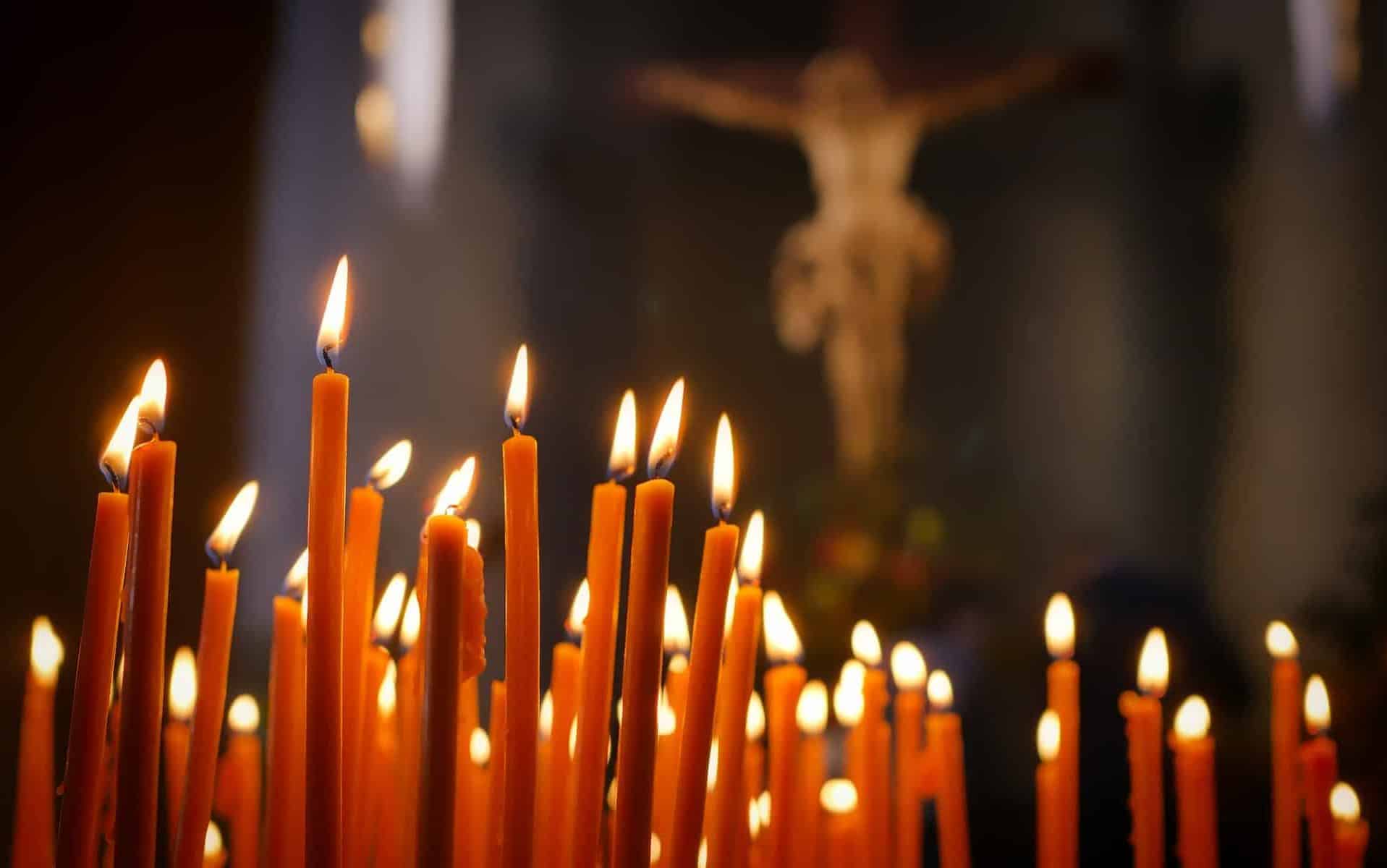 Várias velas acesas e, ao fundo, uma representação/estátua de Jesus Cristo crucificado.