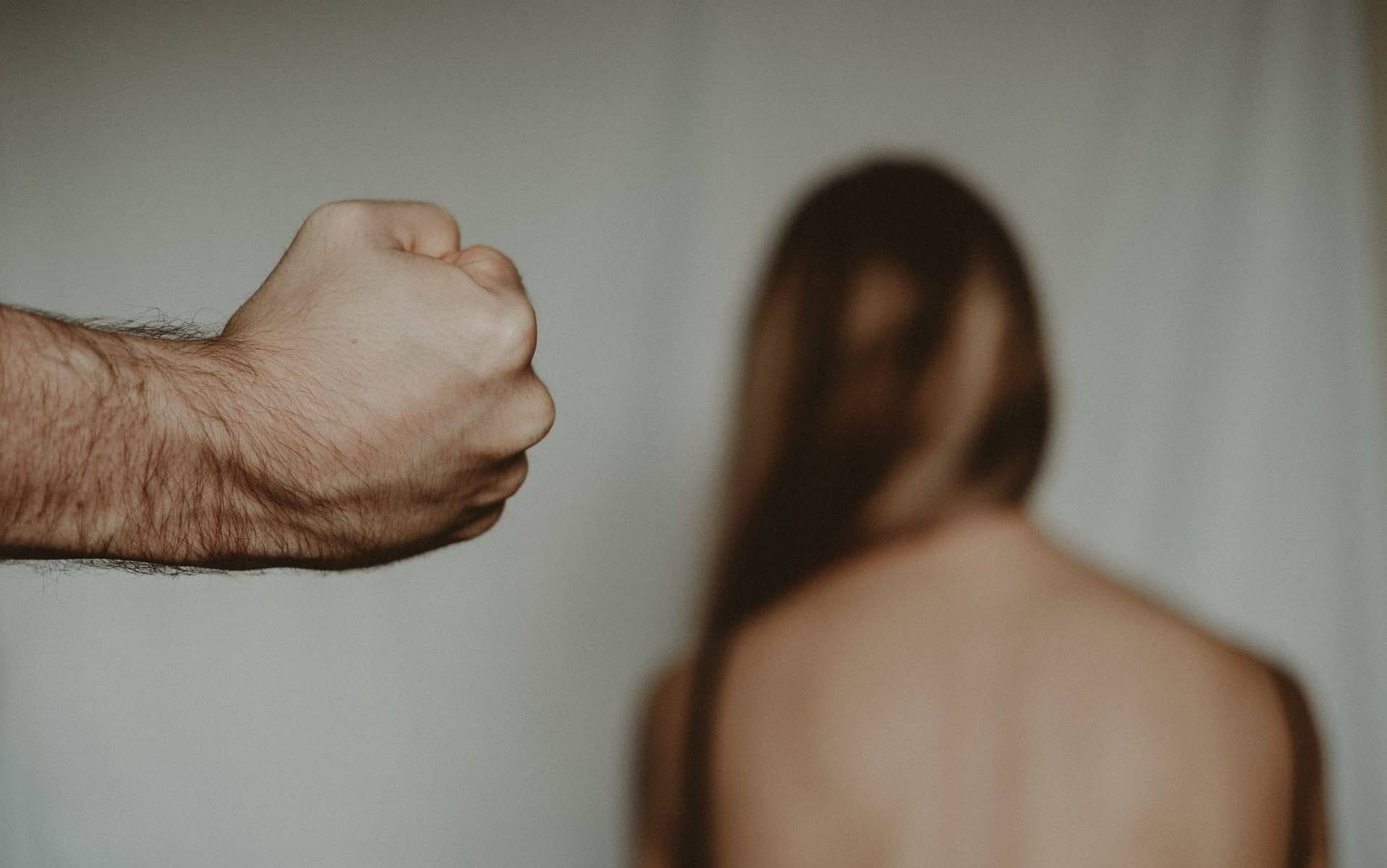 Um punho fechado masculino e, no fundo, uma mulher de costas.