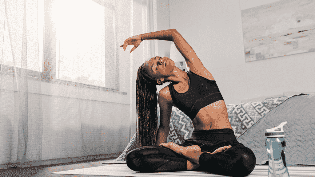 Mulher sentada no chão de um quarto de olhos fechados, praticando yoga