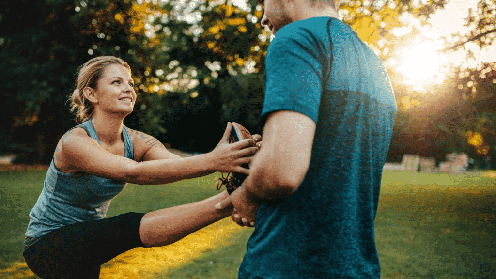 Mulher se alongando com a ajuda de um homem em um parque