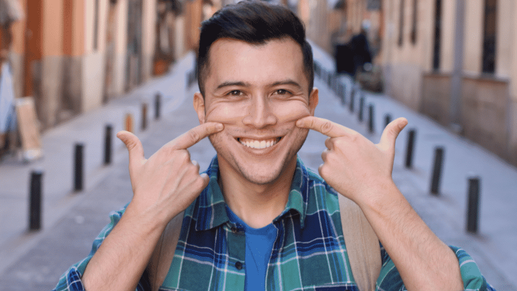 Homem sorrindo e com os dedos empurrando as bochechas para cima