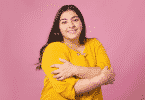 Mulher se abraçando e sorrindo para a foto em um fundo rosa