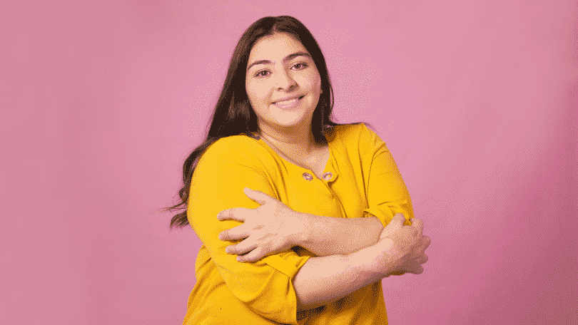 Mulher se abraçando e sorrindo para a foto em um fundo rosa