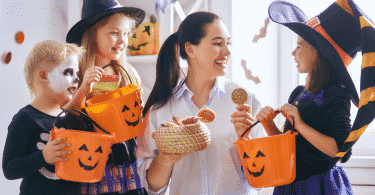Mulher adulta entregando doces para crianças fantasiadas no Halloween