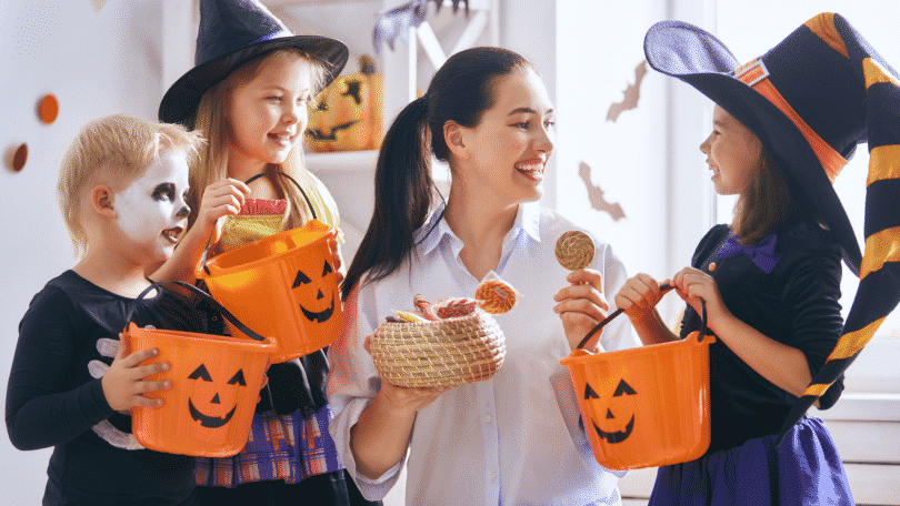 Mulher adulta entregando doces para crianças fantasiadas no Halloween