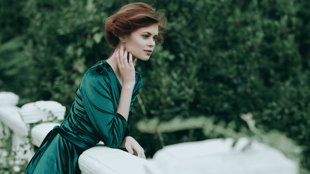 Mulher em uma varanda, usando um vestido verde. Diversas árvores estão a sua volta