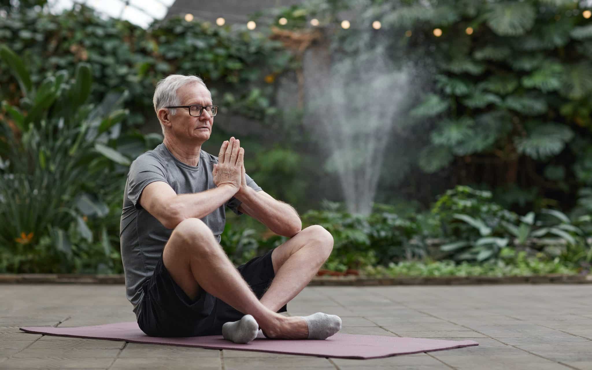 Um homem idoso meditando frente à uma zona verde.