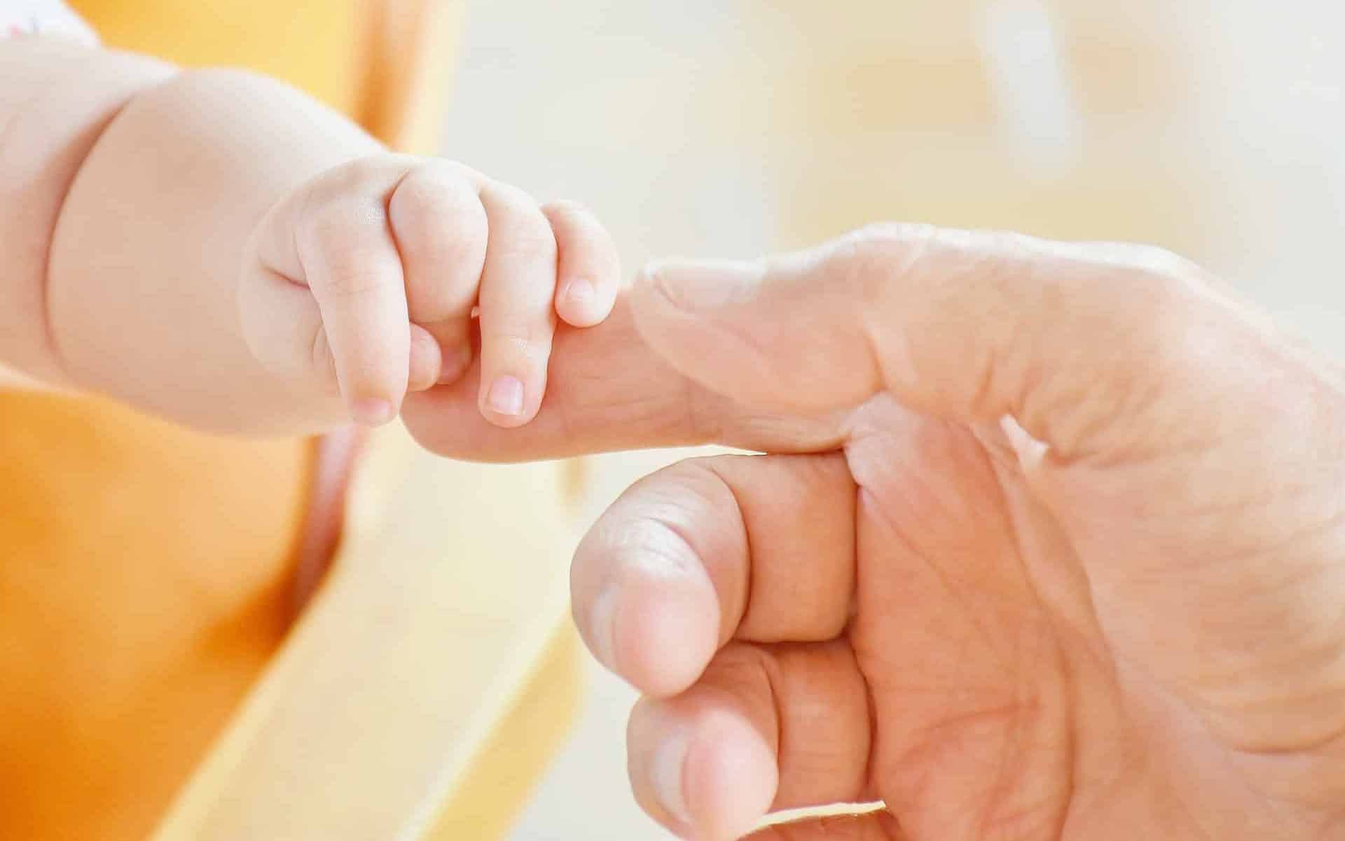 Um mão de um bebê segurando o dedo indicador de uma mão masculina.