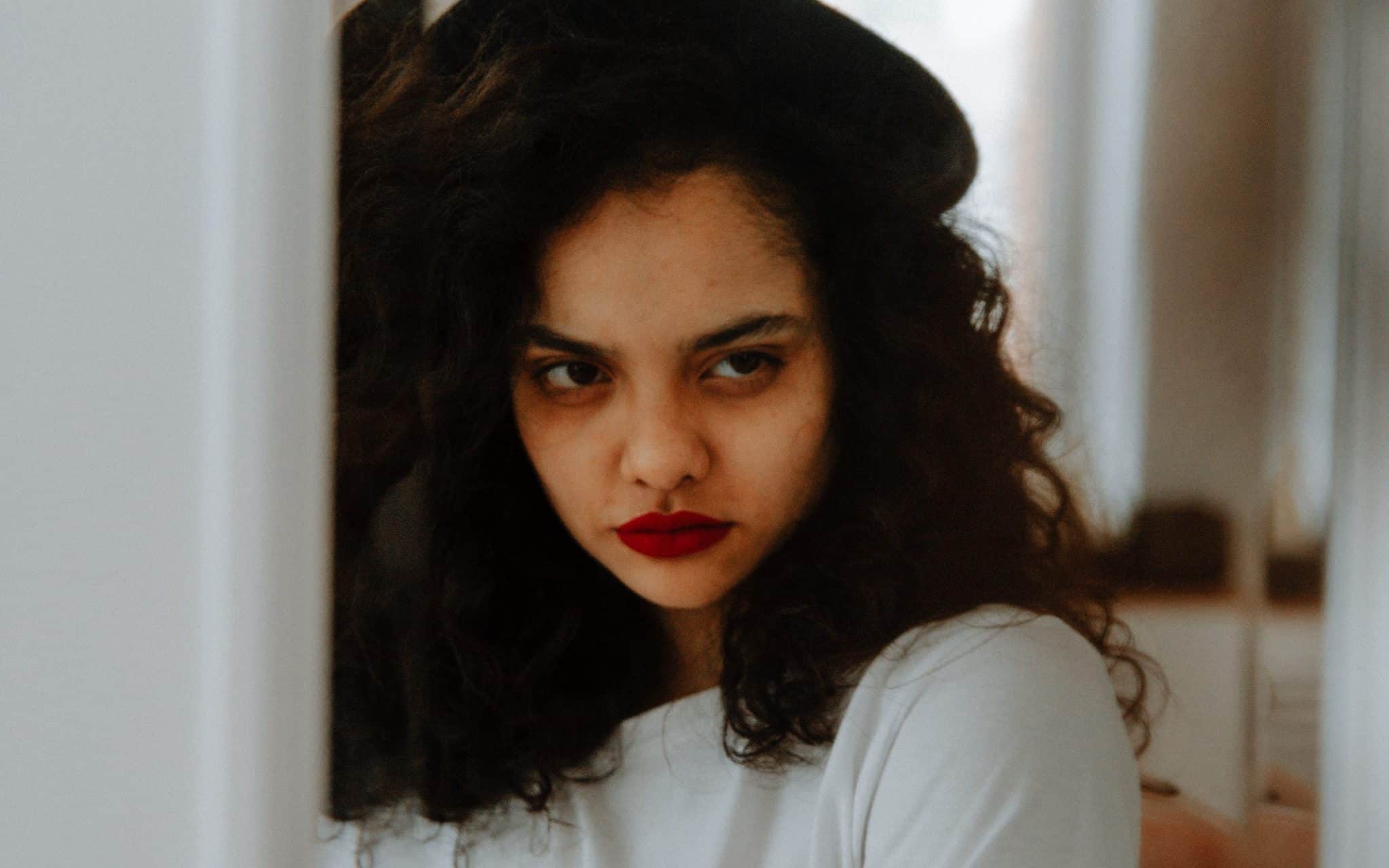 Uma mulher morena olhando para o seu reflexo com um olhar de desaprovação.