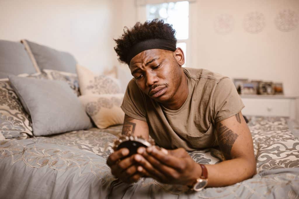Um homem negro deitado de bruços numa cama olhando um porta-retrato. Ele parece estar frustrado.