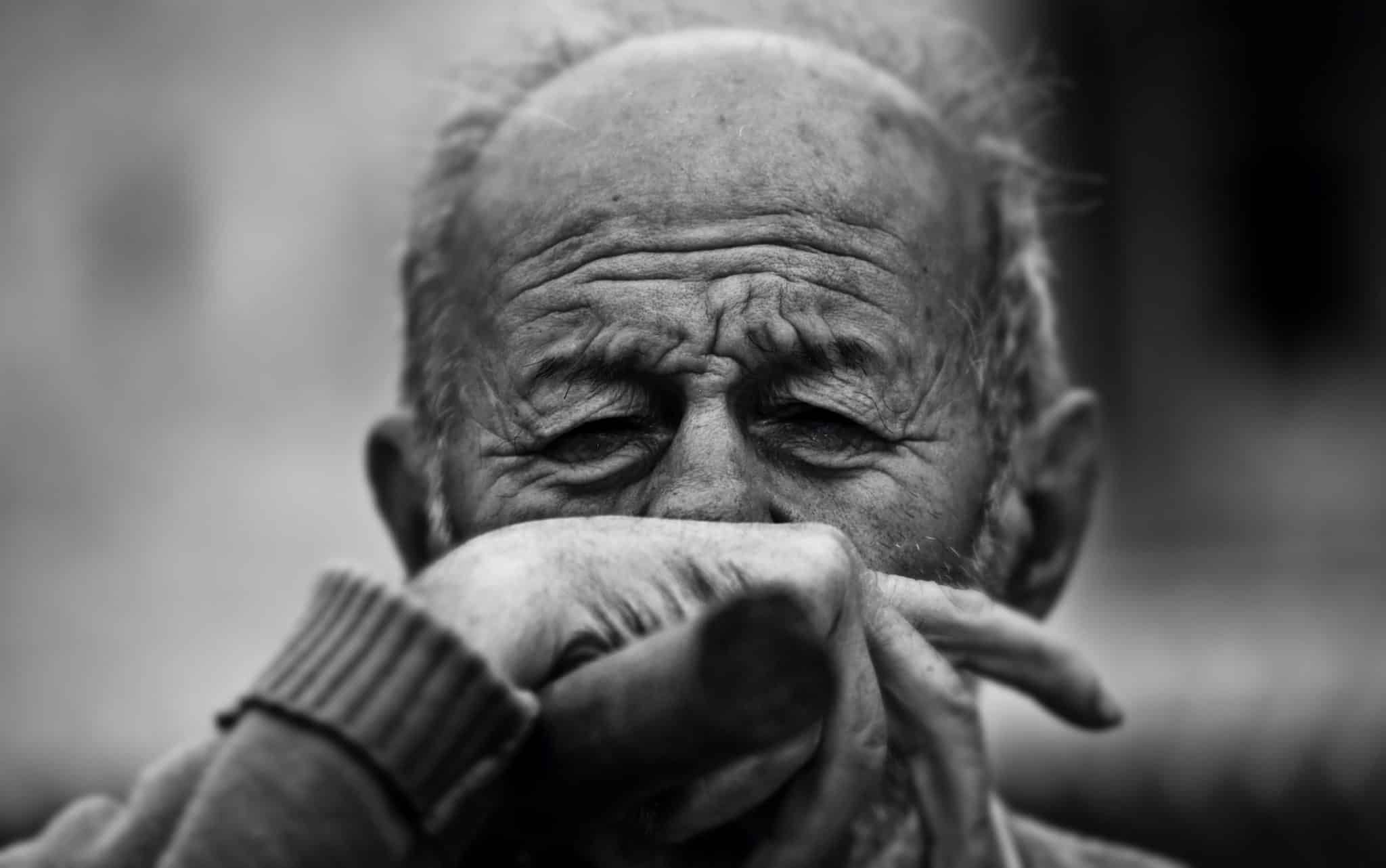 Um homem idoso colocando sua mão sobre o seu rosto.