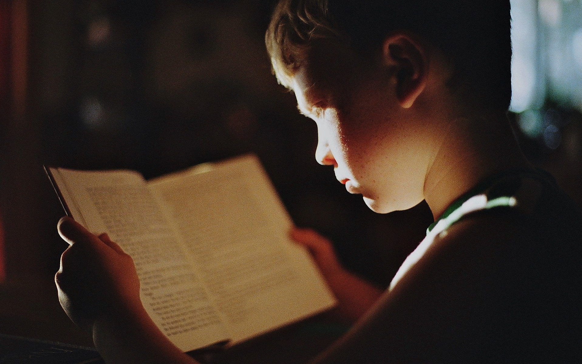 Um garoto lendo um livro. Uma forte fonte de luz é vista sobre o seu rosto.