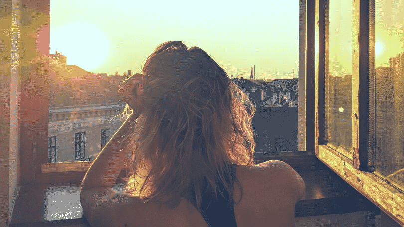 Uma mulher olhando um raio de sol pela janela.
