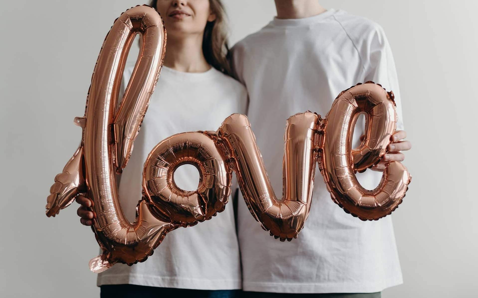 Um homem e uma mulher segurando um balão letrado com a palavra "love".