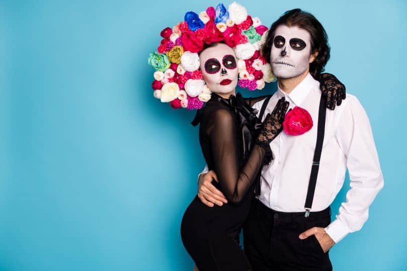 Um homem e uma mulher abraçados e fantasiados com trajes típicos do Día de Los Muertos Mexicano