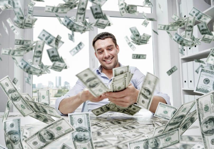 Um homem de negócios - sorrindo - num escritório. Uma grande quantidade de dinheiro caindo sobre o escritório.