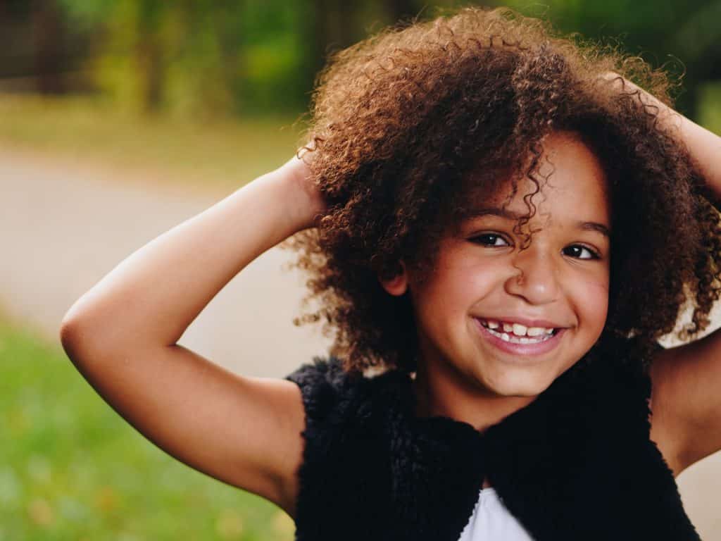 Menina negra sorrindo e com as mãos no cabelo.