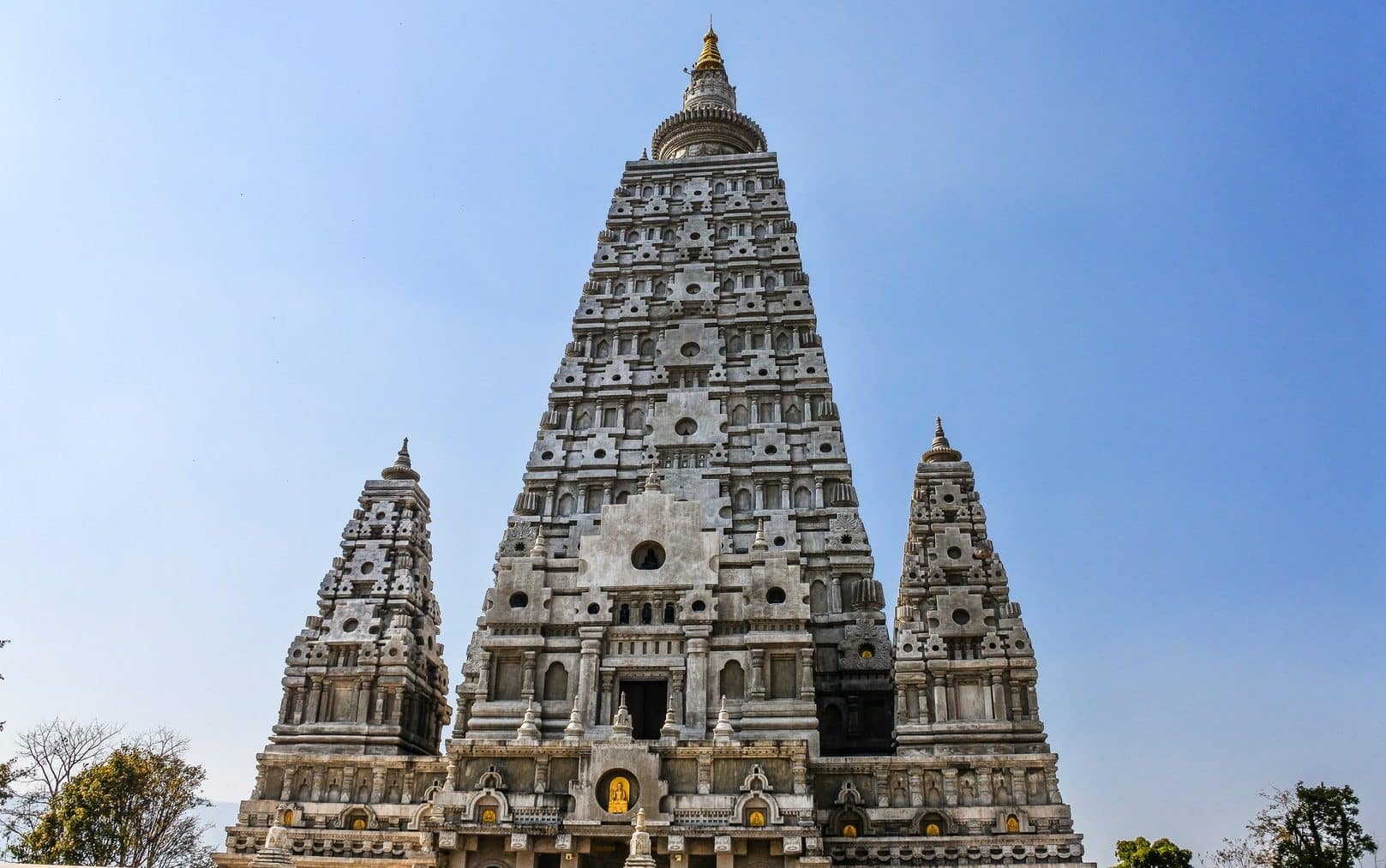 Templo Mahabodhi. Uma construção gigantesca e elevada, com duas pequenas construções auxiliares situadas lateralmente, uma à esquerda, outra à direita.