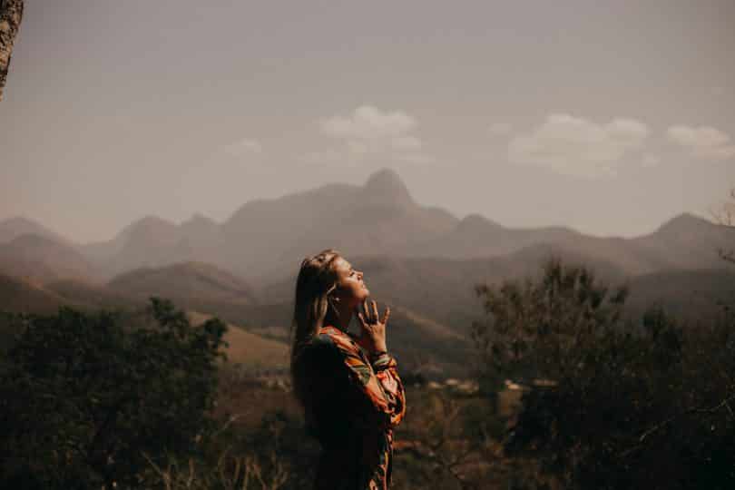 Mulher branca de olhos fechados e mãos juntas num campo.