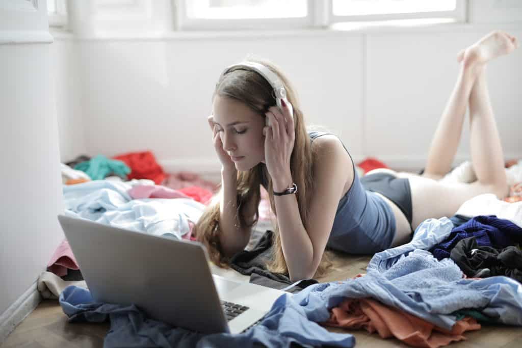 Jovem deitada na cama deitada em sua cama de frente para seu laptop